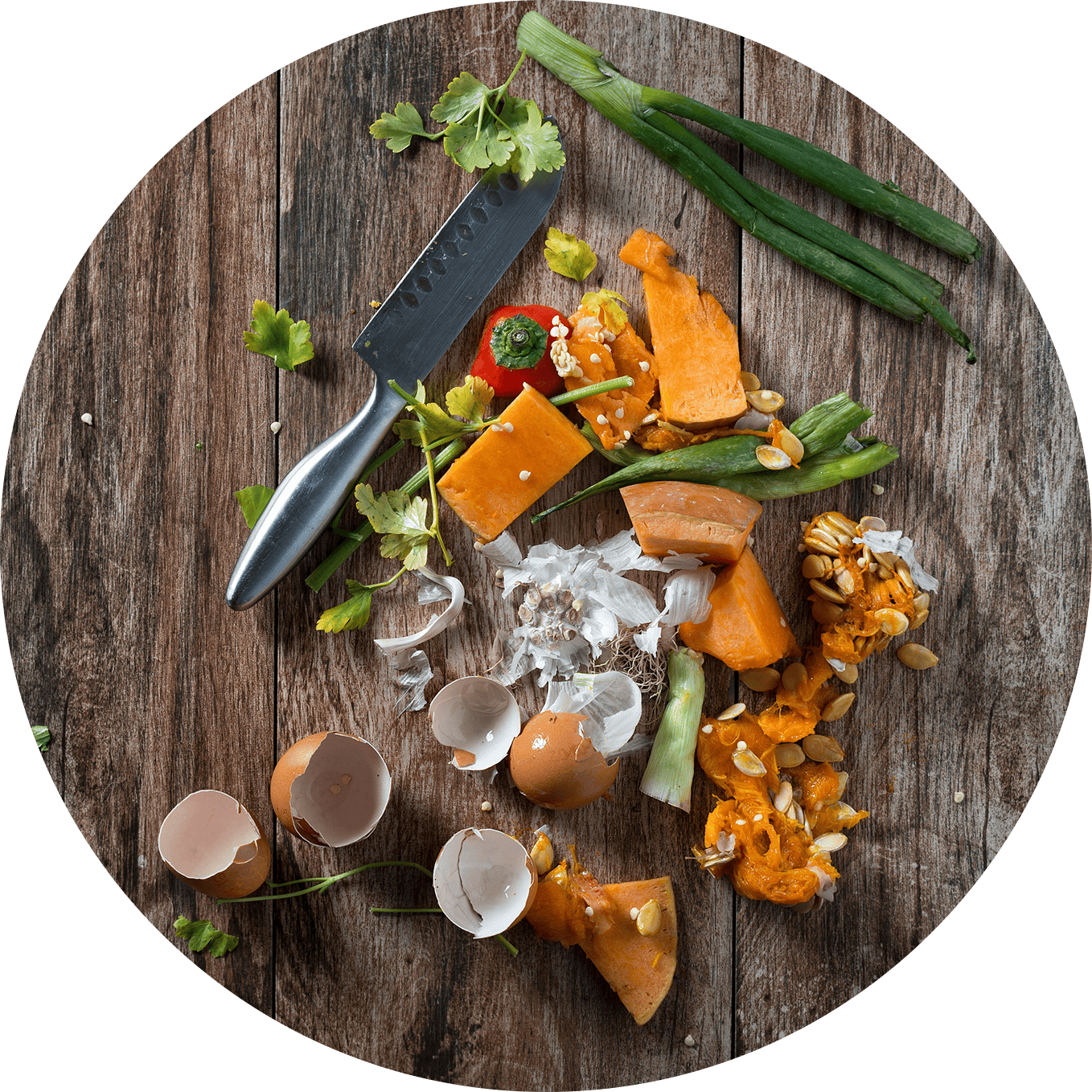 Food waste and organic scraps on a wooden surface with a knife and green onions.