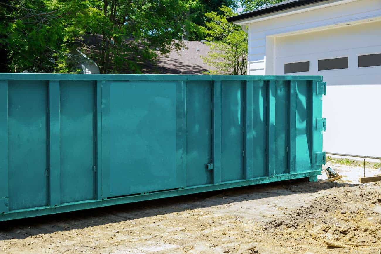 Large teal waste container on construction site for residential and commercial debris removal.