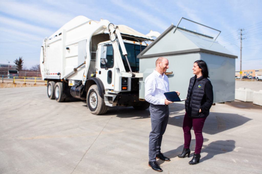 hero image - 2 waste solutions employees in front of garbage truck lifting dumpster