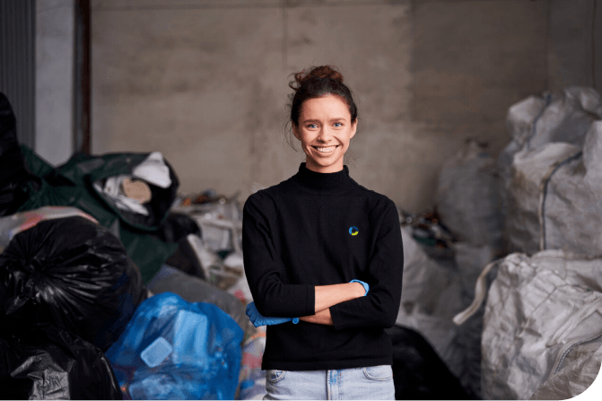 smiling person wearing waste solutions shirt standing in front of waste bags