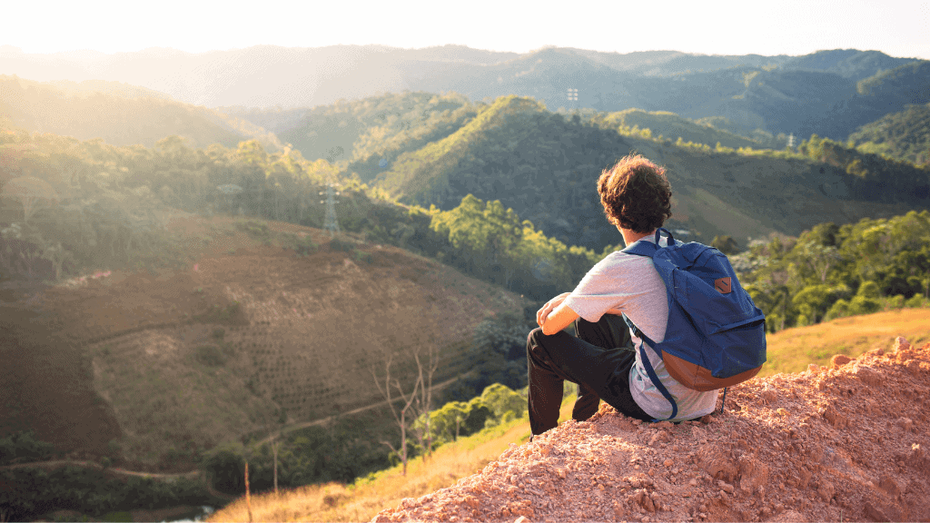 Young person sitting on a hill overlooking lush mountains, highlighting waste management's role in h.