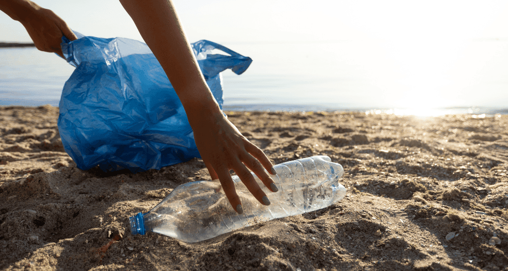 Person discarding plastic bottle on sandy beach for eco-conscious waste management.