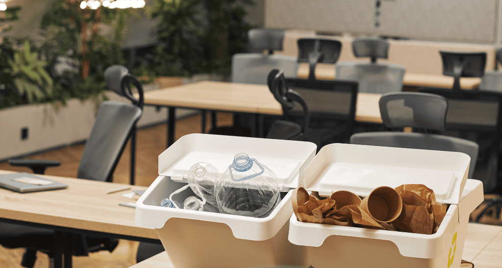 Recycling bins with plastic bottles and paper cups on an outdoor table.