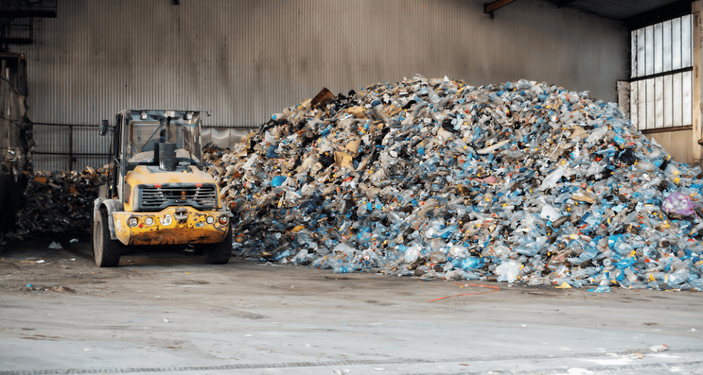 Large pile of plastic waste with a forklift in an industrial warehouse setting.