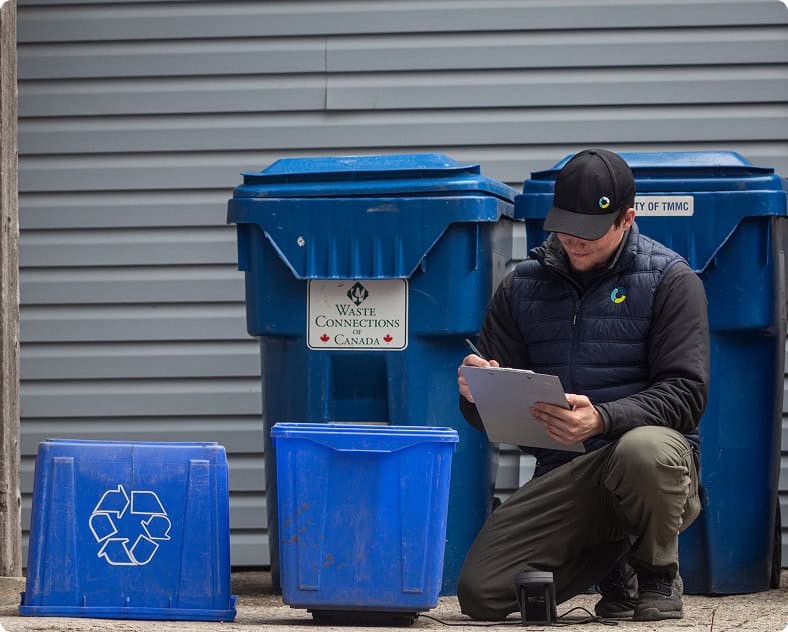 Technician inspecting recycling bins for waste management and recycling compliance.