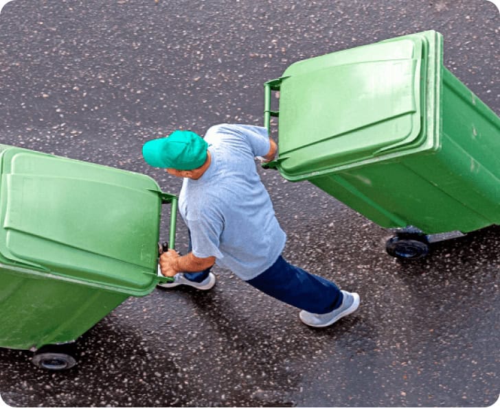 Waste management worker handling green trash bins on street.